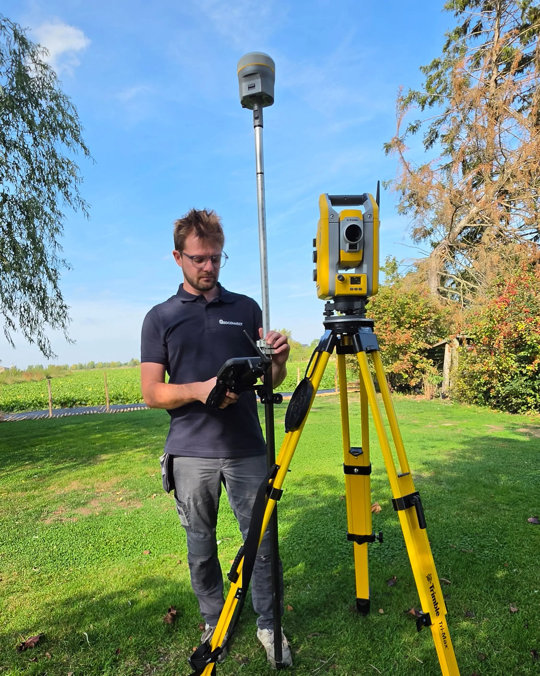 Géomètre de GeoConnect en polo, réglant une station totale Trimble sur trépied en prairie