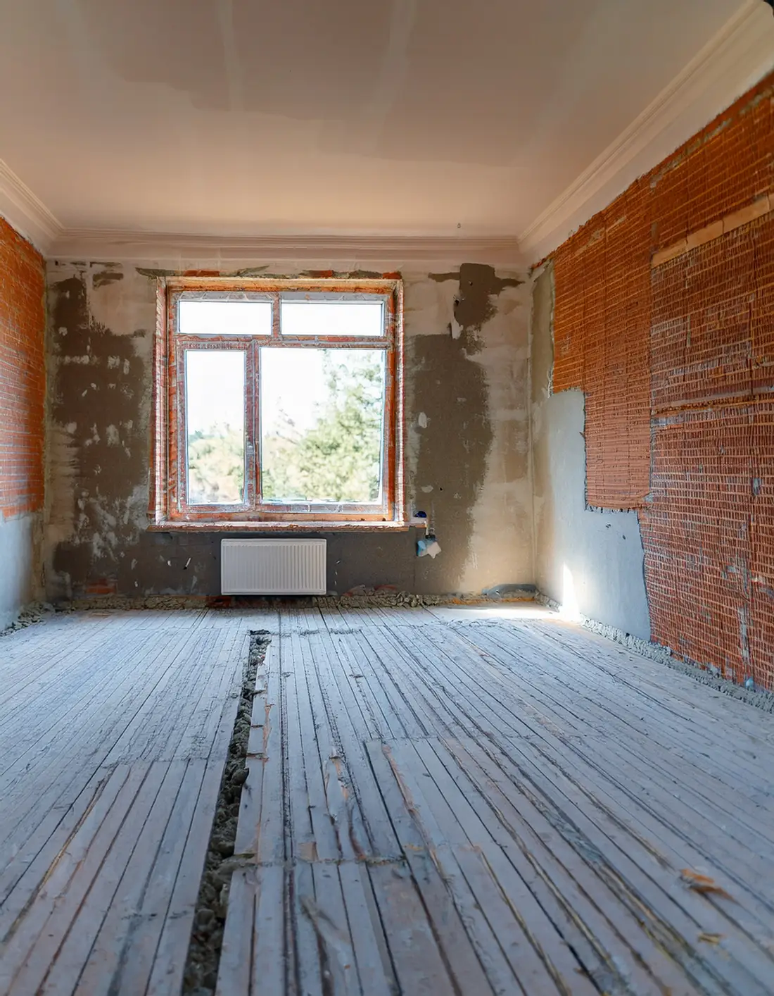 Pièce vide en rénovation : murs décroûtés jusqu’à la brique, corniche de plâtre et plancher de lames ouvert sur une ligne